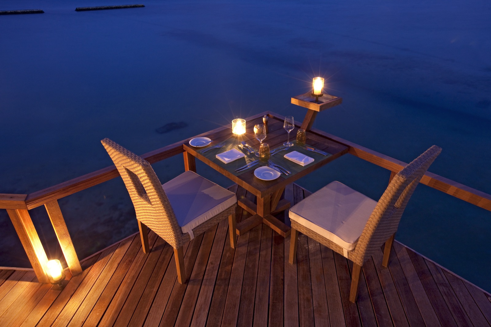 Table dressée pour deux sur un deck en bois au-dessus de l'océan, photographiée de nuit