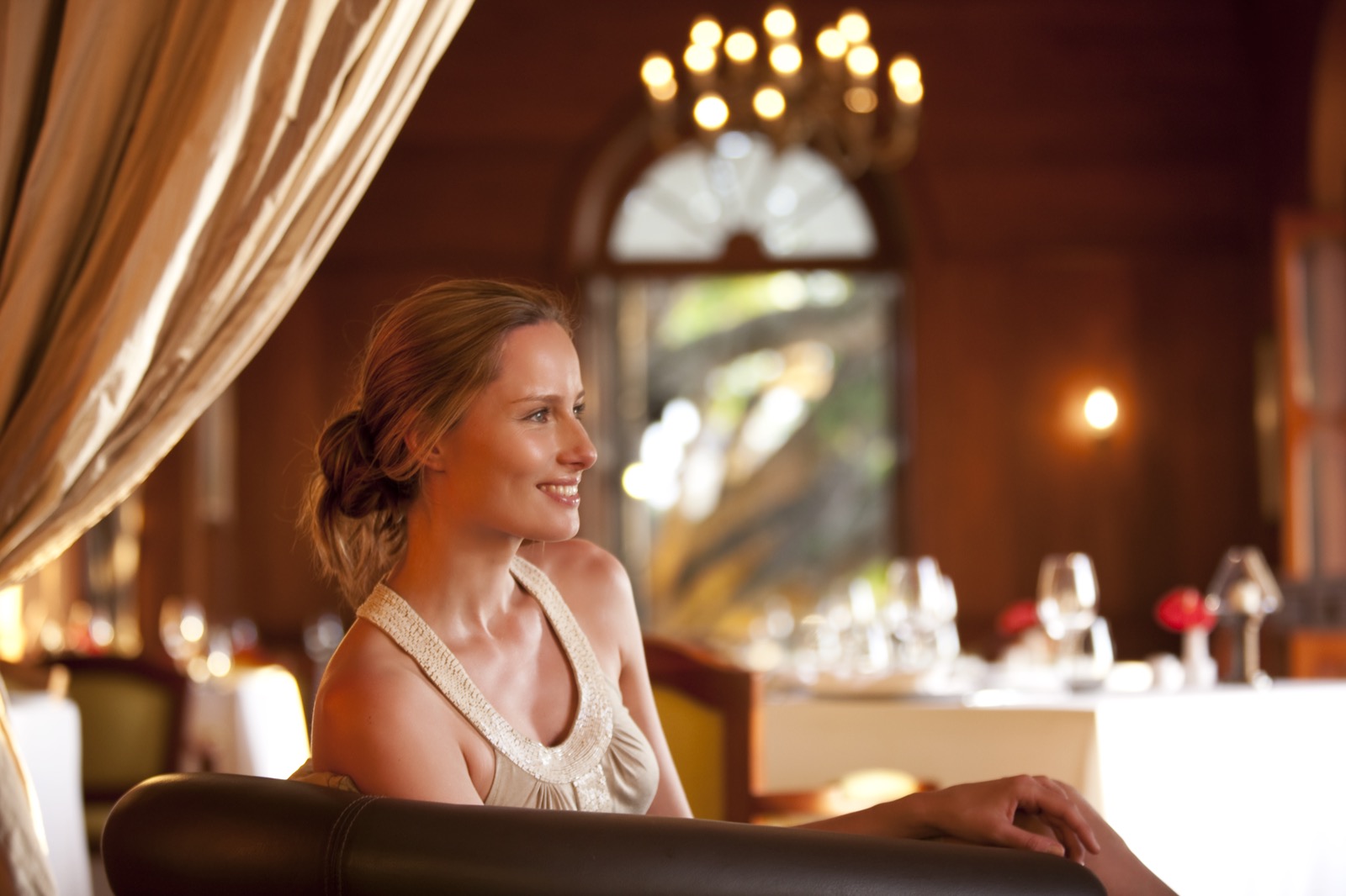 Une femme seule dans une salle de restaurant gastronomique à l'éclairage chaud et feutré, boiseries sombres