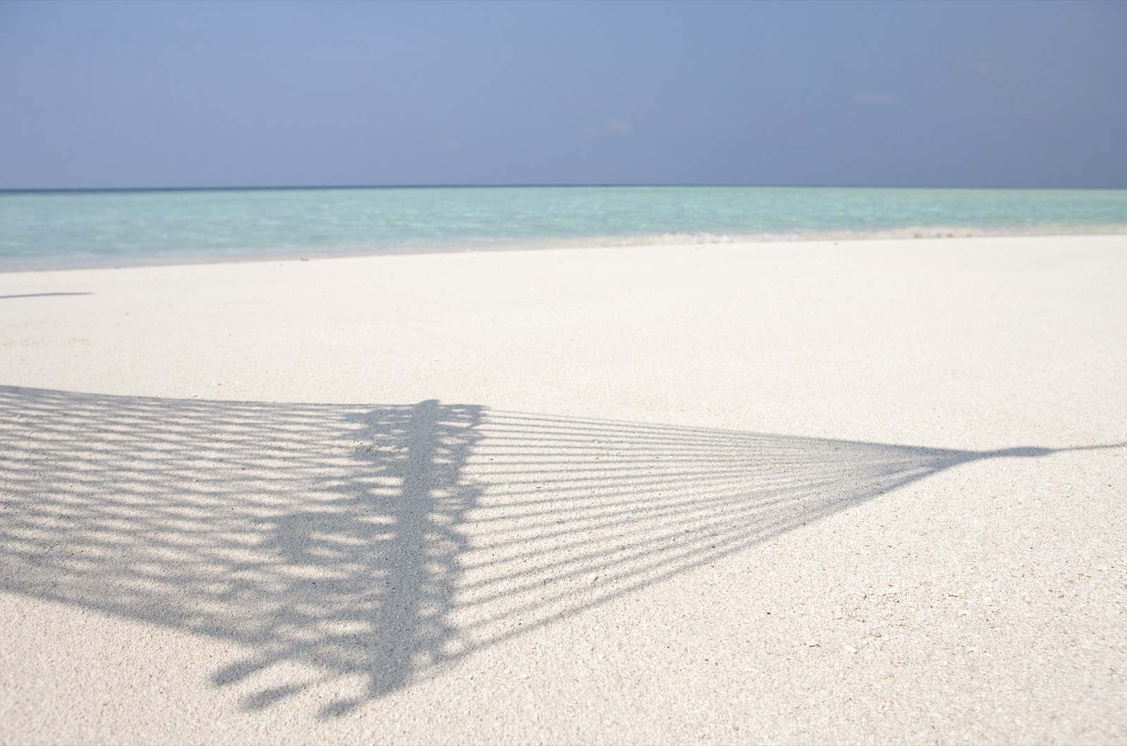 Ombre d'un hamac en filet projetée sur du sable blanc fin, mer turquoise en arrière-plan