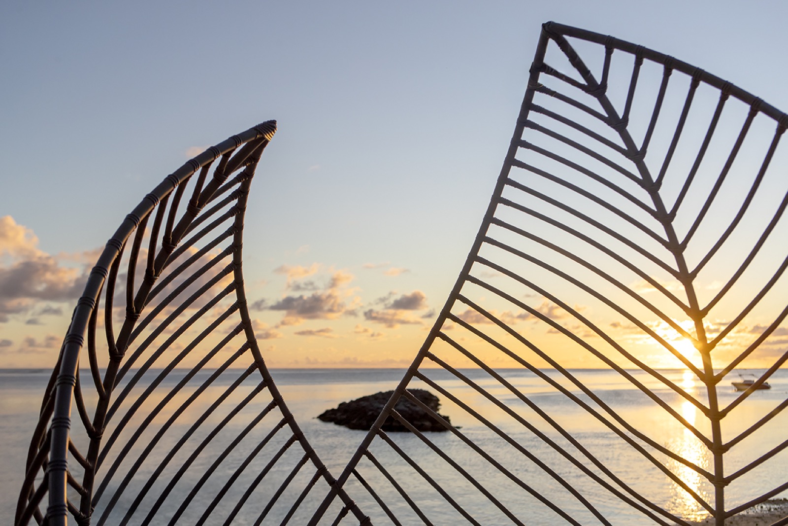 Deux sculptures en métal forgé en forme de feuilles encadrent un coucher de soleil sur l'océan