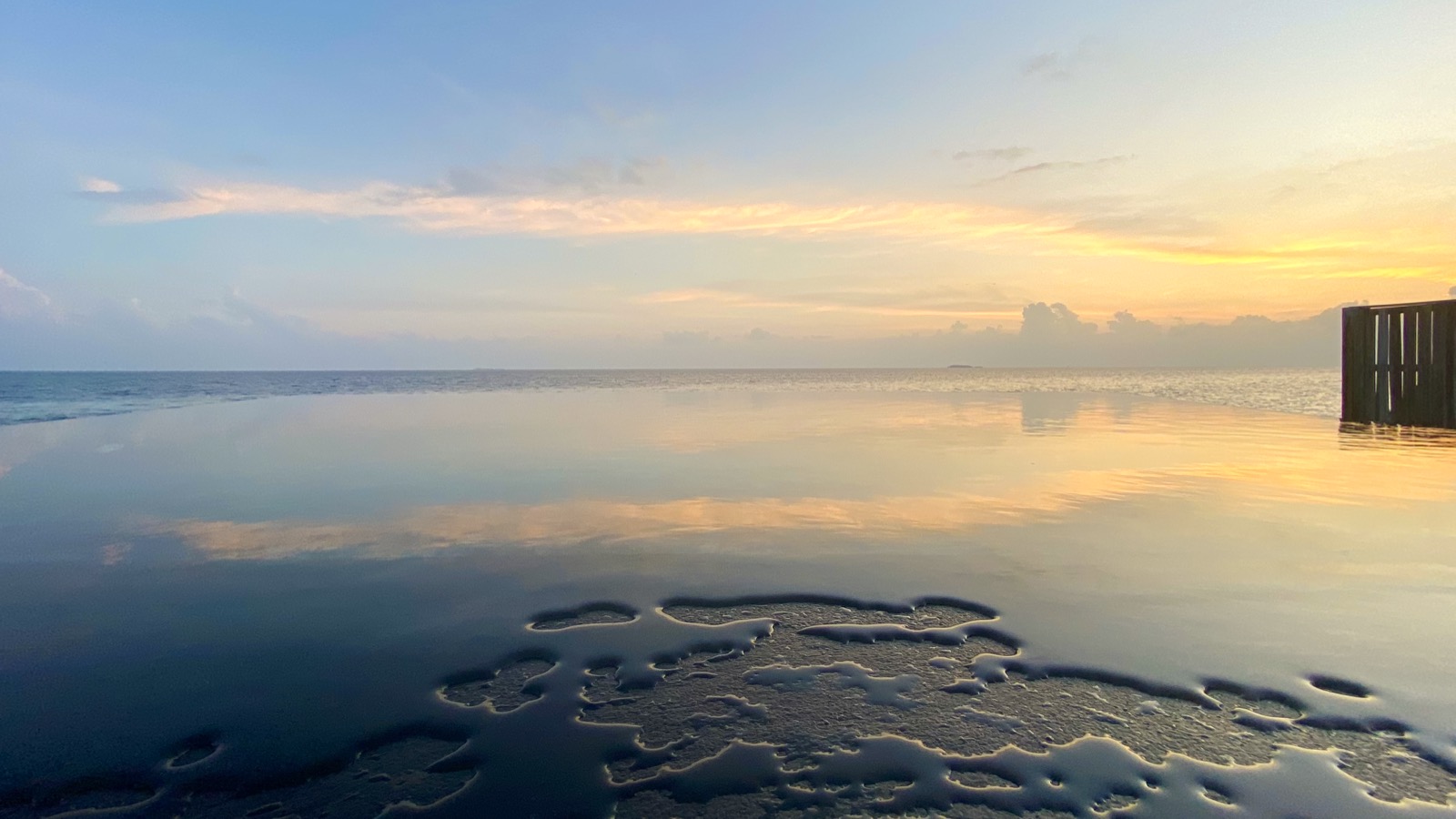 Piscine à débordement au crépuscule, surface immobile reflétant le ciel orangé du coucher de soleil