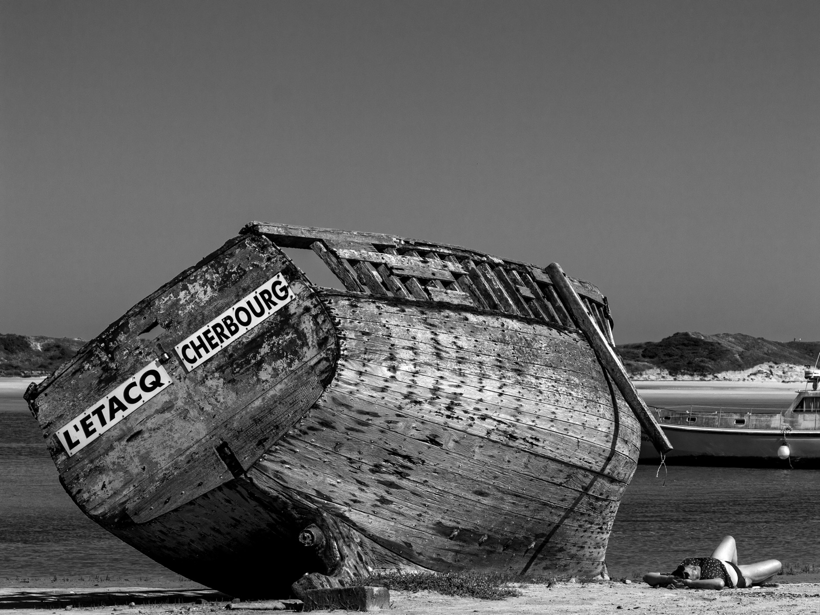 Vieux bateau de pêche en bois échoué sur le sable, coque marquée L'Étacq Cherbourg, photographie en noir et blanc